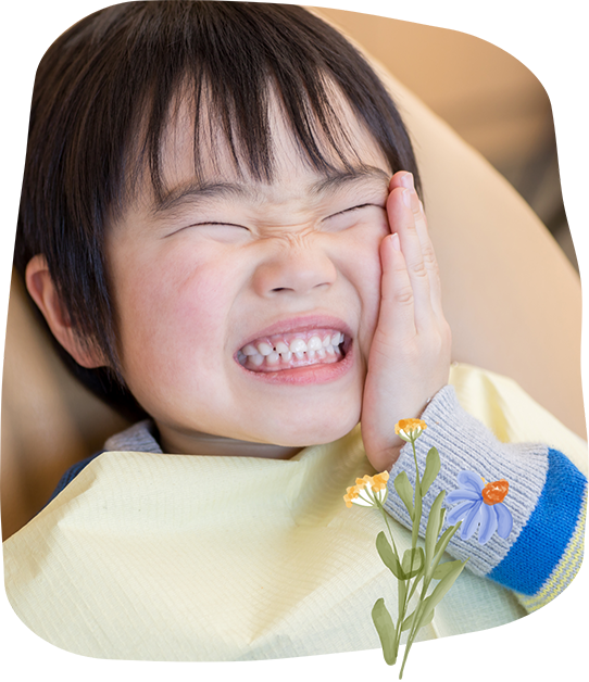 Child in the dental chair wincing and holding the side of their face in pain